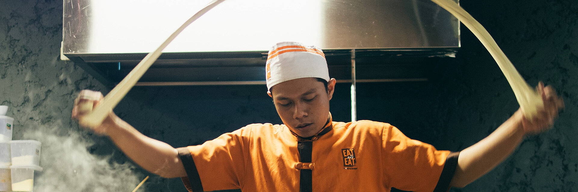 [Translate to Italienisch:] Asian cook with embroidered working shirt