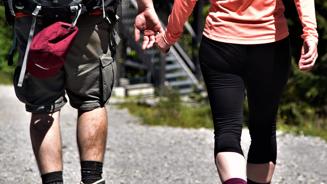 Two people in sportswear holding hands and walking on a hiking trail