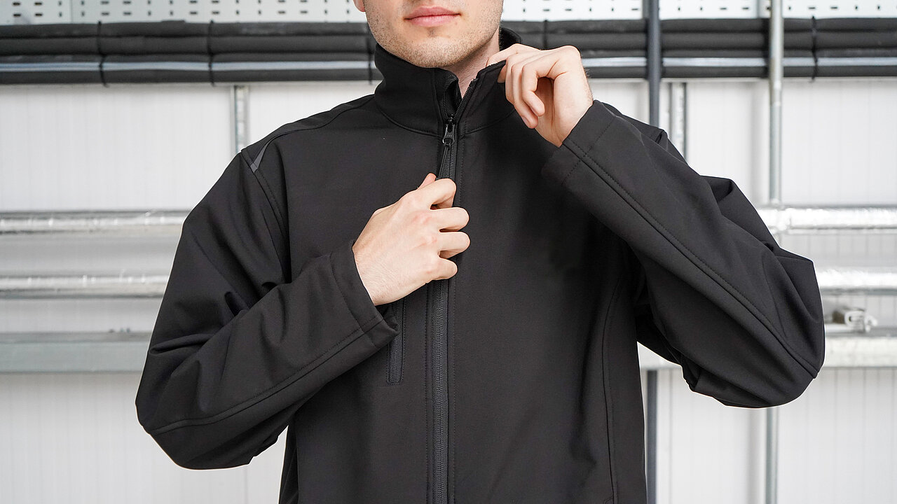 A person in a black softshell jacket against a grey background