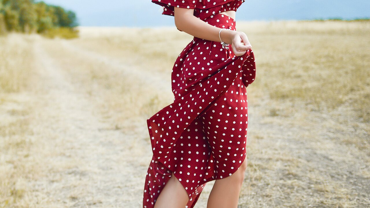 Uma pessoa com um vestido vermelho com pontos brancos num campo amarelo